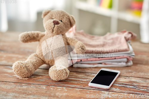 Image of baby clothes, teddy bear toy and smartphone