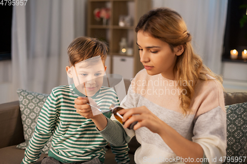 Image of mother giving medication or cough syrup to ill son