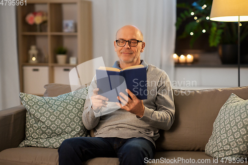 Image of happy bald senior man on sofa reading book at home