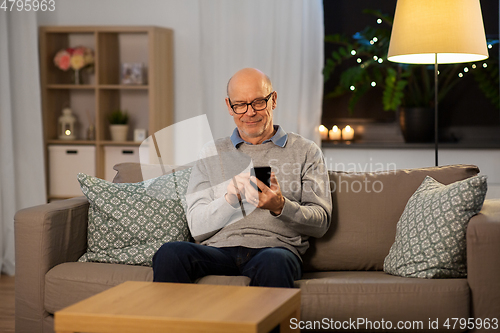 Image of happy senior man texting on smartphone at home