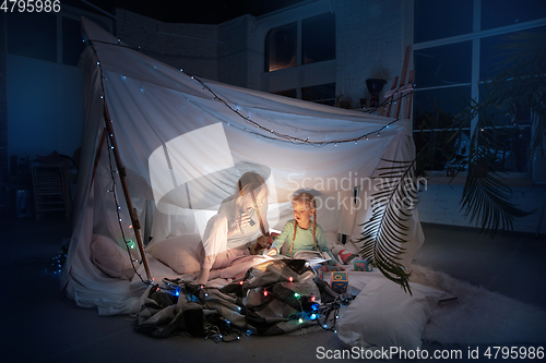 Image of Mother and daughter sitting in a teepee, reading stories with the flashlight