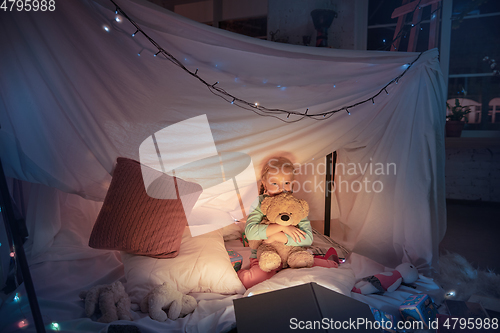 Image of Little girl lying in a teepee, playing with the flashlight