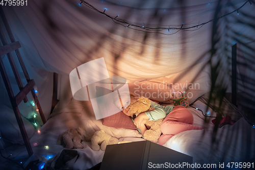 Image of Little girl lying in a teepee, playing with the flashlight