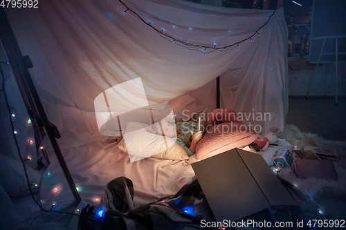 Image of Little girl lying in a teepee, playing with the flashlight