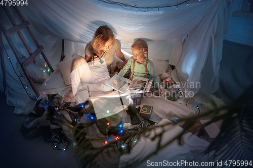 Image of Mother and daughter sitting in a teepee, reading stories with the flashlight