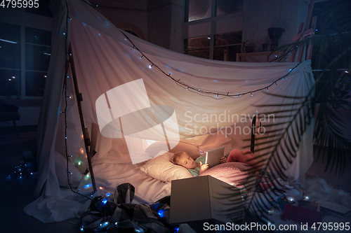 Image of Little girl lying in a teepee, playing with the flashlight