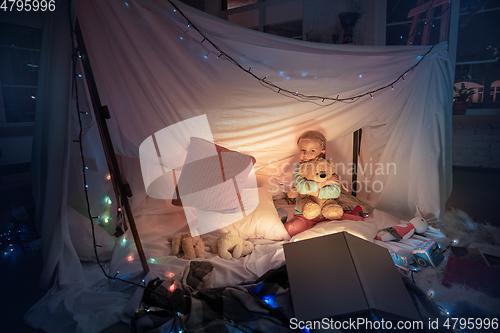 Image of Little girl lying in a teepee, playing with the flashlight