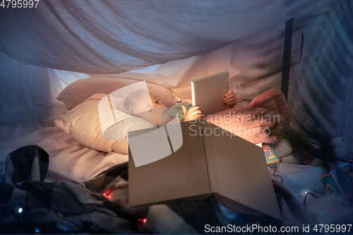 Image of Little girl lying in a teepee, playing with the flashlight