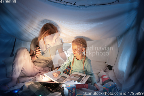 Image of Mother and daughter sitting in a teepee, reading stories with the flashlight