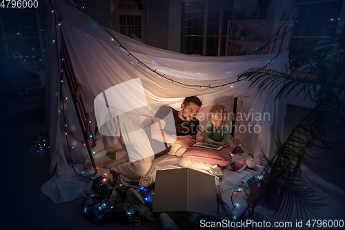 Image of Father and daughter sitting in a teepee, having fun with the flashlight