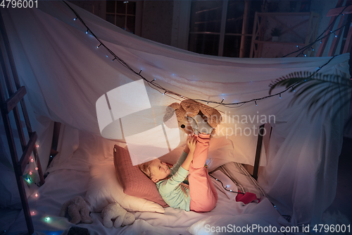 Image of Little girl lying in a teepee, playing with the flashlight