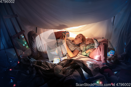 Image of Mother and daughter sitting in a teepee, having fun with the flashlight