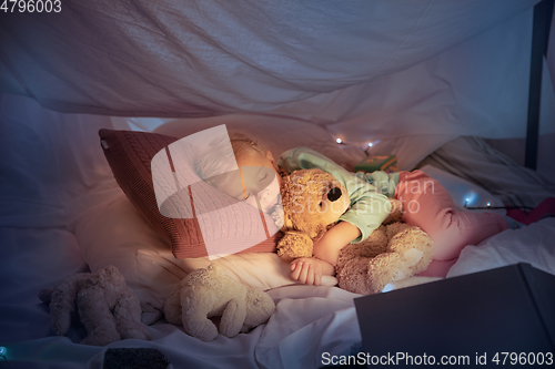 Image of Little girl lying in a teepee, sleeping with the flashlight