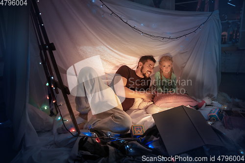 Image of Father and daughter sitting in a teepee, having fun with the flashlight