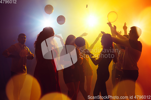 Image of A crowd of people in silhouette raises their hands against colorful neon light on party background