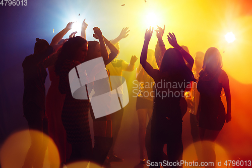 Image of A crowd of people in silhouette raises their hands against colorful neon light on party background