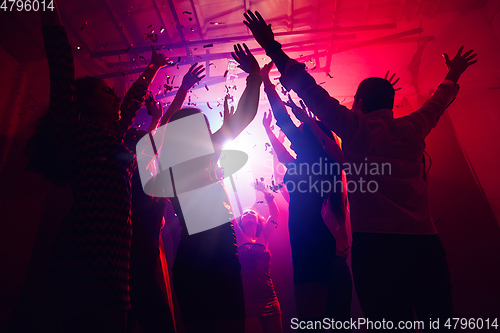 Image of A crowd of people in silhouette raises their hands against colorful neon light on party background