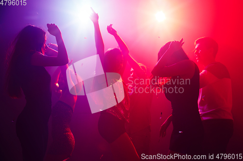 Image of A crowd of people in silhouette raises their hands against colorful neon light on party background