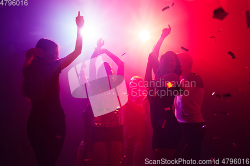 Image of A crowd of people in silhouette raises their hands against colorful neon light on party background