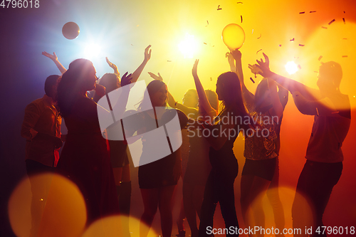 Image of A crowd of people in silhouette raises their hands against colorful neon light on party background