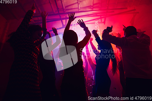 Image of A crowd of people in silhouette raises their hands against colorful neon light on party background