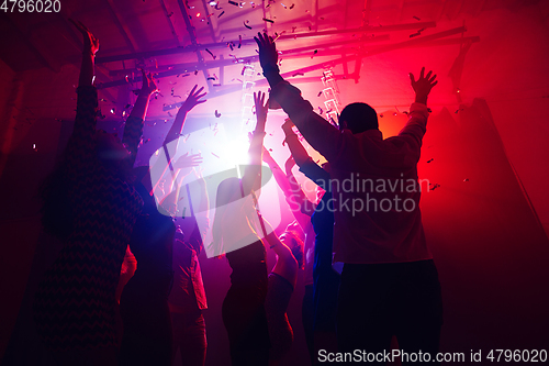 Image of A crowd of people in silhouette raises their hands against colorful neon light on party background