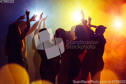 Image of A crowd of people in silhouette raises their hands against colorful neon light on party background