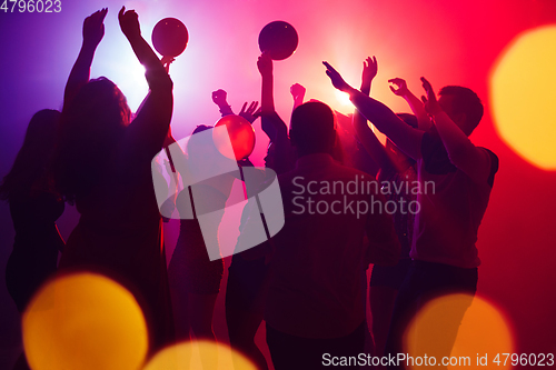 Image of A crowd of people in silhouette raises their hands against colorful neon light on party background