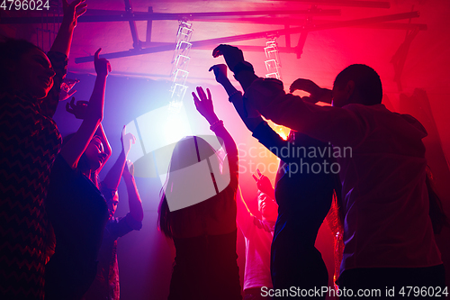 Image of A crowd of people in silhouette raises their hands against colorful neon light on party background