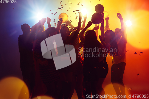 Image of A crowd of people in silhouette raises their hands against colorful neon light on party background