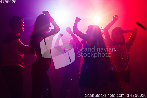 Image of A crowd of people in silhouette raises their hands against colorful neon light on party background