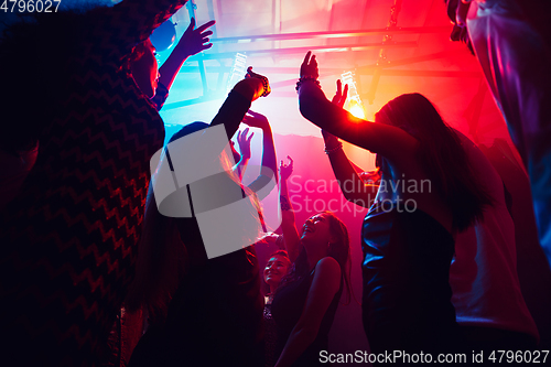 Image of A crowd of people in silhouette raises their hands against colorful neon light on party background