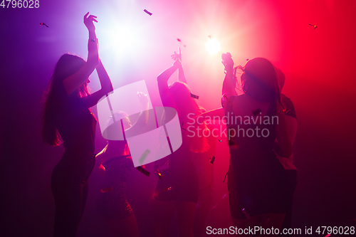 Image of A crowd of people in silhouette raises their hands against colorful neon light on party background