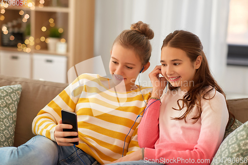 Image of happy girls with smartphone and earphones at home