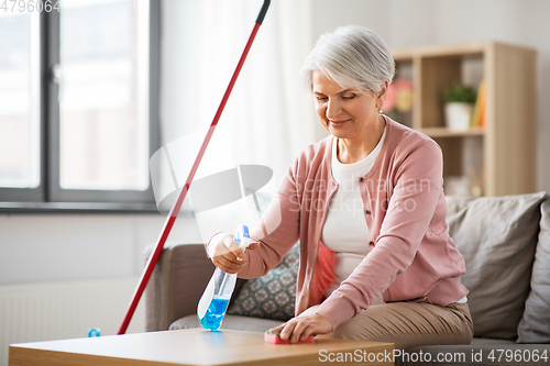 Image of senior woman with detergent cleaning table at home