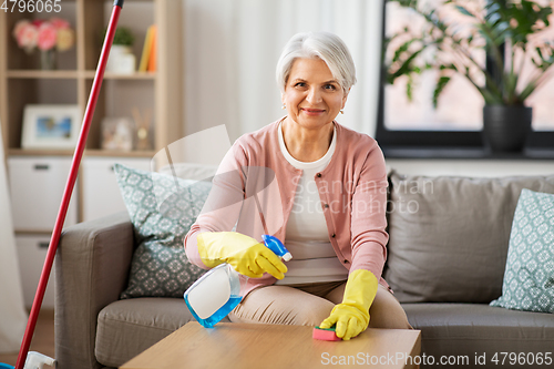 Image of senior woman with detergent cleaning table at home