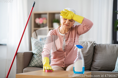 Image of tired senior woman cleaning table at home