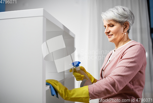 Image of senior woman cleaning rack with detergent at home