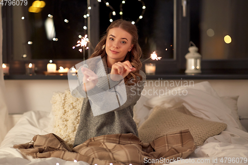 Image of happy young woman with sparklers in bed at home