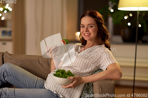 Image of happy smiling pregnant woman eating salad at home