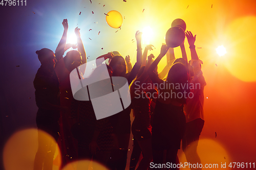 Image of A crowd of people in silhouette raises their hands against colorful neon light on party background