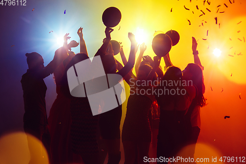 Image of A crowd of people in silhouette raises their hands against colorful neon light on party background