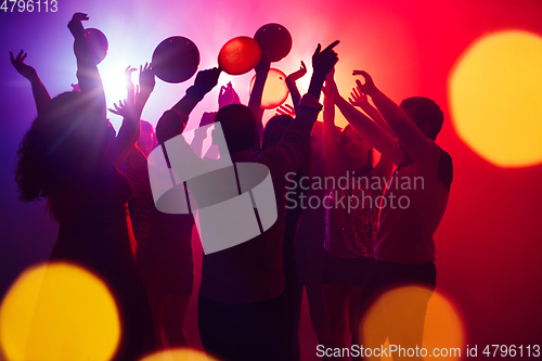 Image of A crowd of people in silhouette raises their hands against colorful neon light on party background