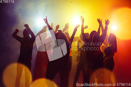 Image of A crowd of people in silhouette raises their hands against colorful neon light on party background