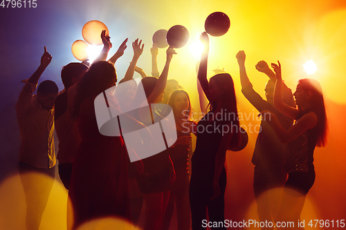 Image of A crowd of people in silhouette raises their hands against colorful neon light on party background