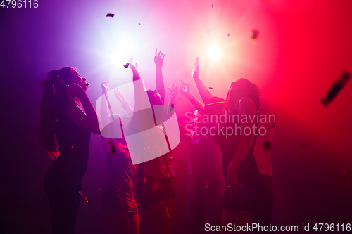 Image of A crowd of people in silhouette raises their hands against colorful neon light on party background