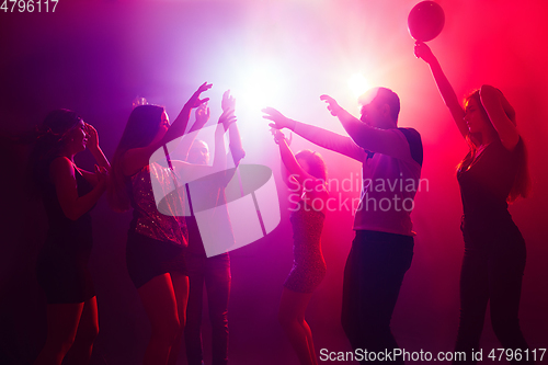 Image of A crowd of people in silhouette raises their hands against colorful neon light on party background