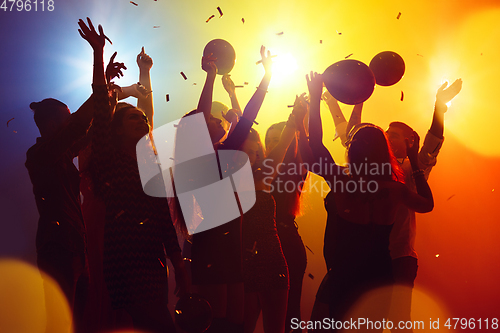 Image of A crowd of people in silhouette raises their hands against colorful neon light on party background