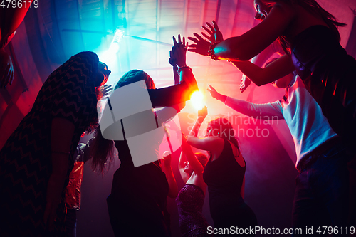 Image of A crowd of people in silhouette raises their hands against colorful neon light on party background