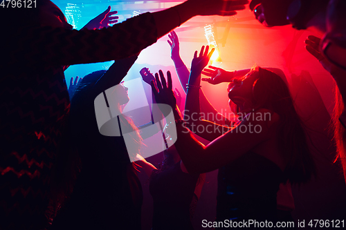 Image of A crowd of people in silhouette raises their hands against colorful neon light on party background